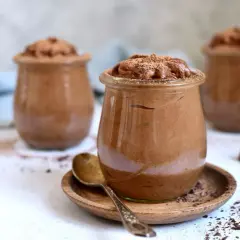 Szybki krem czekoladowy z mascarpone w słoiczkach, posypany kakao. Obok leży tabliczka czekolady.