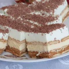 Szybkie ciasto bez pieczenia z budyniem i herbatnikami, przełożone kremem i posypane czekoladą. Idealne na deser.