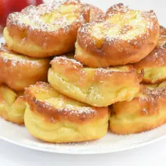 Stos puszystych racuchów na kefirze jak u babci, posypanych cukrem pudrem. Obok jabłka.