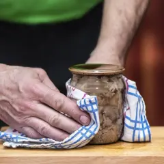 Mężczyzna używa ściereczki, by łatwiej otworzyć słoik z mięsem.