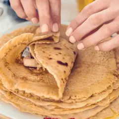 Dłonie zwijają naleśnika z bananem i kremem na talerzu.