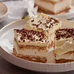 Mega szybkie ciasto bez pieczenia, warstwowe, z kremem i posypką czekoladową, na talerzu z kwiatem.