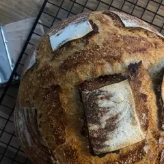 Chleb pszenno żytni na zakwasie, pachnący świeżością, czeka na rozkrojenie. Obok pędzel do smarowania.