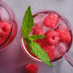Orzeźwiająca lemoniada malinowa z lodem i listkami mięty w szklanych kieliszkach.