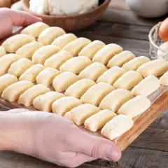 Ania gotuje pierogi leniwe. Na desce ułożone są rzędy gotowych do gotowania pierogów leniwych.