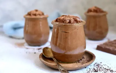 Szybki krem czekoladowy z mascarpone w słoiczkach, posypany kakao. Obok leży tabliczka czekolady.