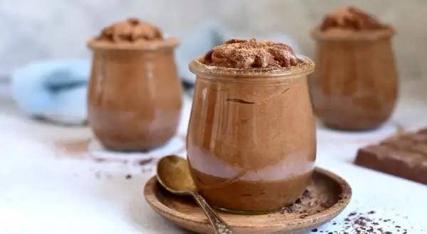 Szybki krem czekoladowy z mascarpone w słoiczkach, posypany kakao. Obok leży tabliczka czekolady.