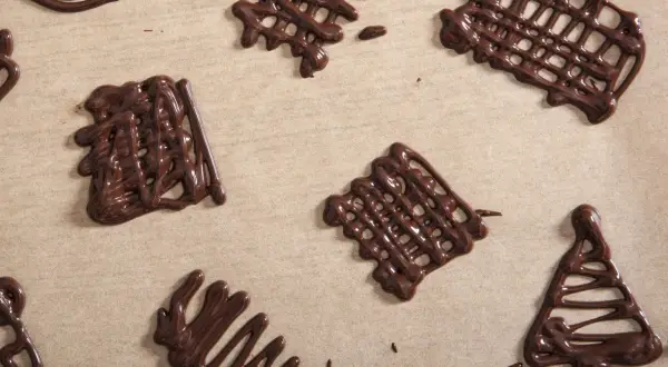 Czekoladowe ozdoby na tort w kształcie siatek i choinki, wykonane na papierze do pieczenia.