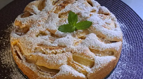 Szybkie tanie ciasto z jabłkami, posypane cukrem pudrem i ozdobione listkiem mięty. Idealne na deser.