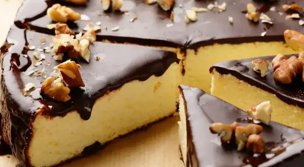 Puszysty sernik z polewą czekoladową z czekolady, ozdobiony orzechami włoskimi.