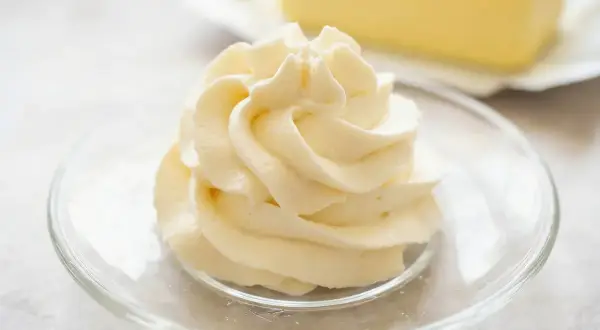 Puszysta masa budyniowa z mascarpone, udekorowana na talerzyku. W tle kostka masła.