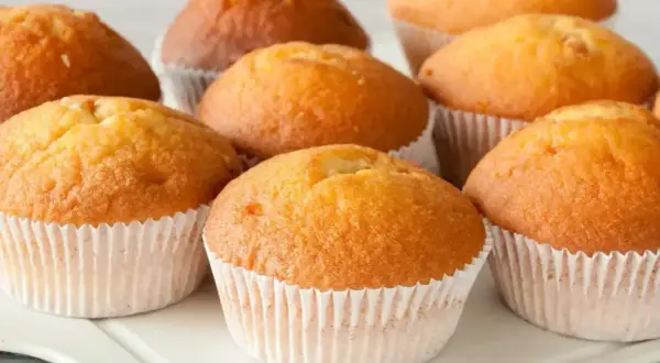 Kilka puszystych, złotobrązowych muffinek w papierowych foremkach na białej tacy.