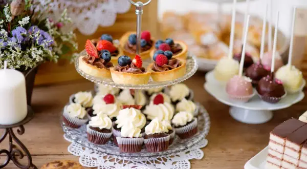 Słodkie przekąski: babeczki, tartaletki z owocami, cake pops i ciasto czekoladowe na drewnianym stole.