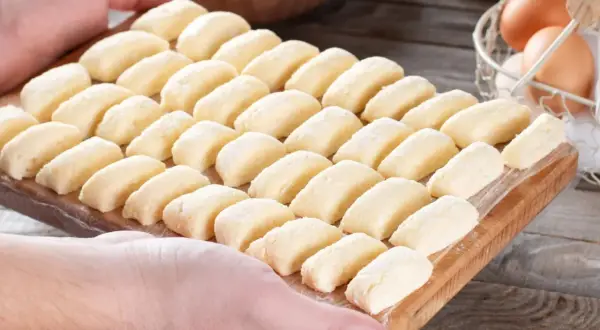 Ania gotuje pierogi leniwe. Na desce ułożone są rzędy gotowych do gotowania pierogów leniwych.