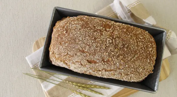 Gotowy do pieczenia chleb orkiszowy na drożdżach w keksówce, posypany ziarnami. Idealny przepis na zdrowe śniadanie.