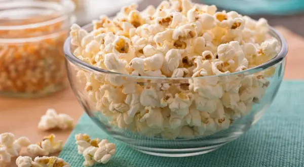 Puszysty popcorn na patelni, gotowy do chrupania. W tle widać nasiona kukurydzy.