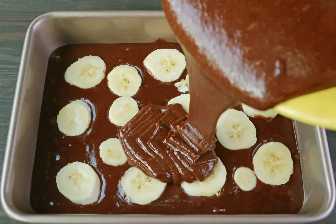 Czekoladowy deser z bananami w trakcie przygotowania. Ciasto wylewane jest do formy z plasterkami banana.