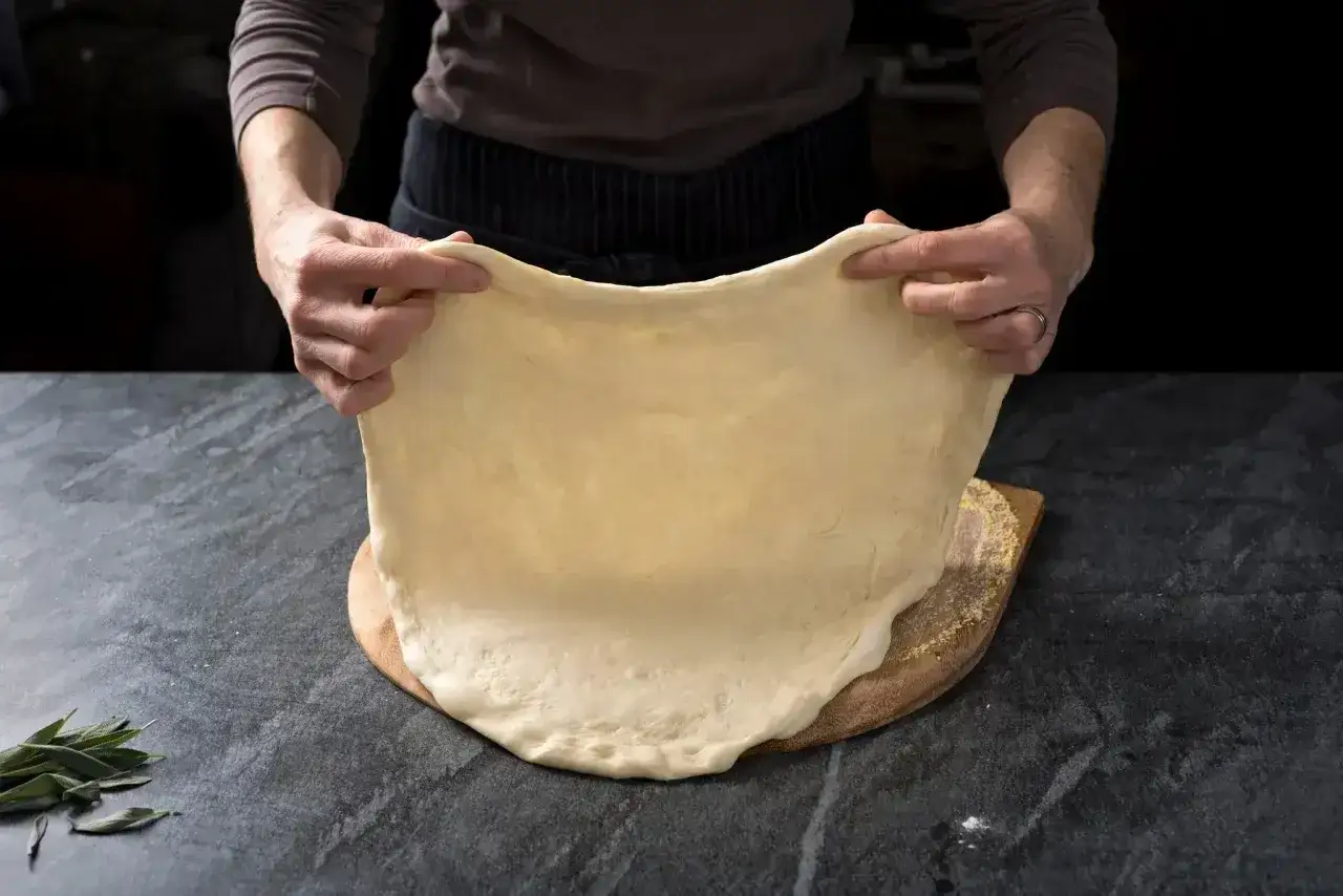 Ręce rozciągają elastyczne ciasto na pizzę, przygotowując je do pieczenia. Idealny przepis na ciasto do pizzy.