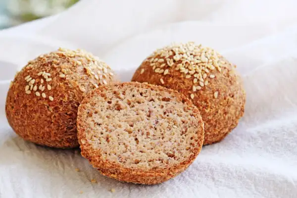 Proste keto bułki z sezamem, jedna przekrojona, ukazująca puszyste wnętrze. Idealne na dietę ketogeniczną.