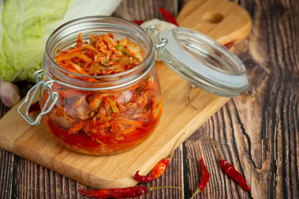 Słoik z domowym kimchi, idealny do przepisów na przetwory domowe. Obok kapusta, czosnek i papryczki chili.