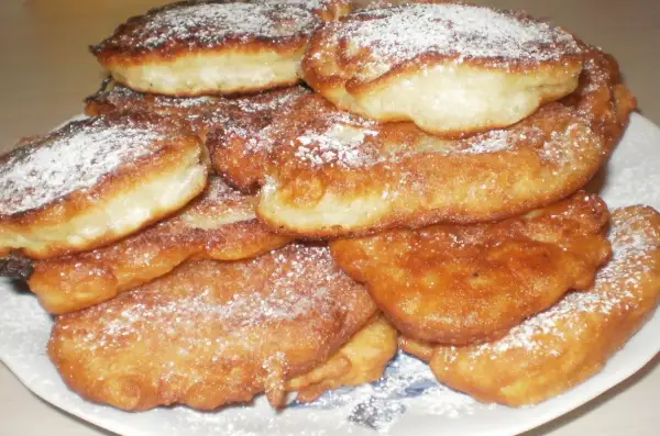 Stos puszystych, złotych racuchów z jabłkami, posypanych cukrem pudrem.