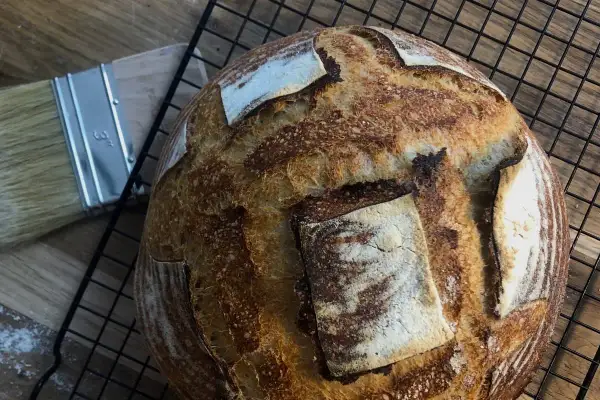 Chleb pszenno żytni na zakwasie, pachnący świeżością, czeka na rozkrojenie. Obok pędzel do smarowania.