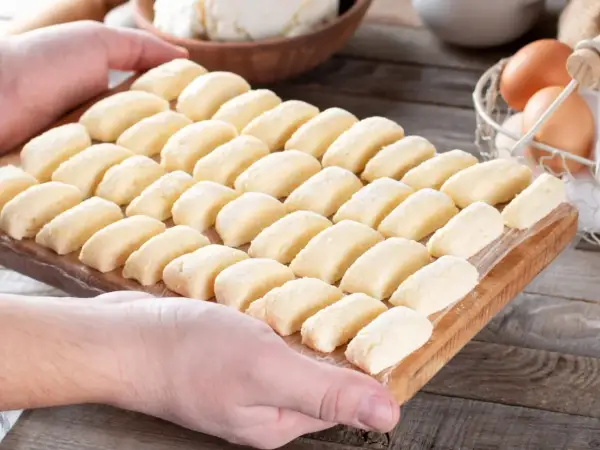 Ania gotuje pierogi leniwe. Na desce ułożone są rzędy gotowych do gotowania pierogów leniwych.
